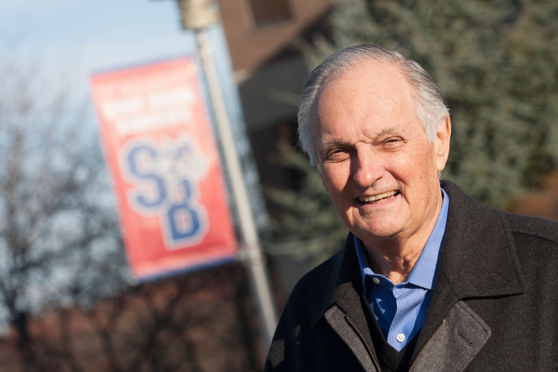 Alan Alda ouside on campus in front of Stony Brook banner