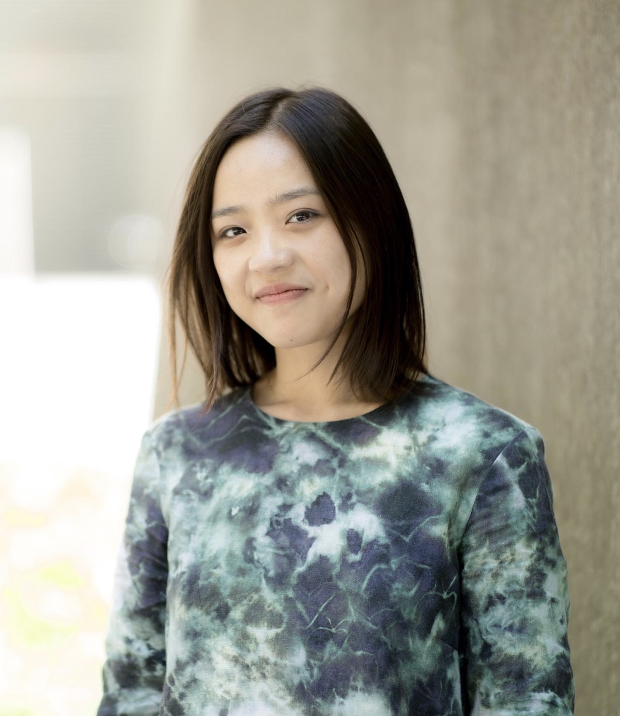 Jenny Tang Portrait of a person smiling, wearing a tie-dye shirt, standing outdoors.
