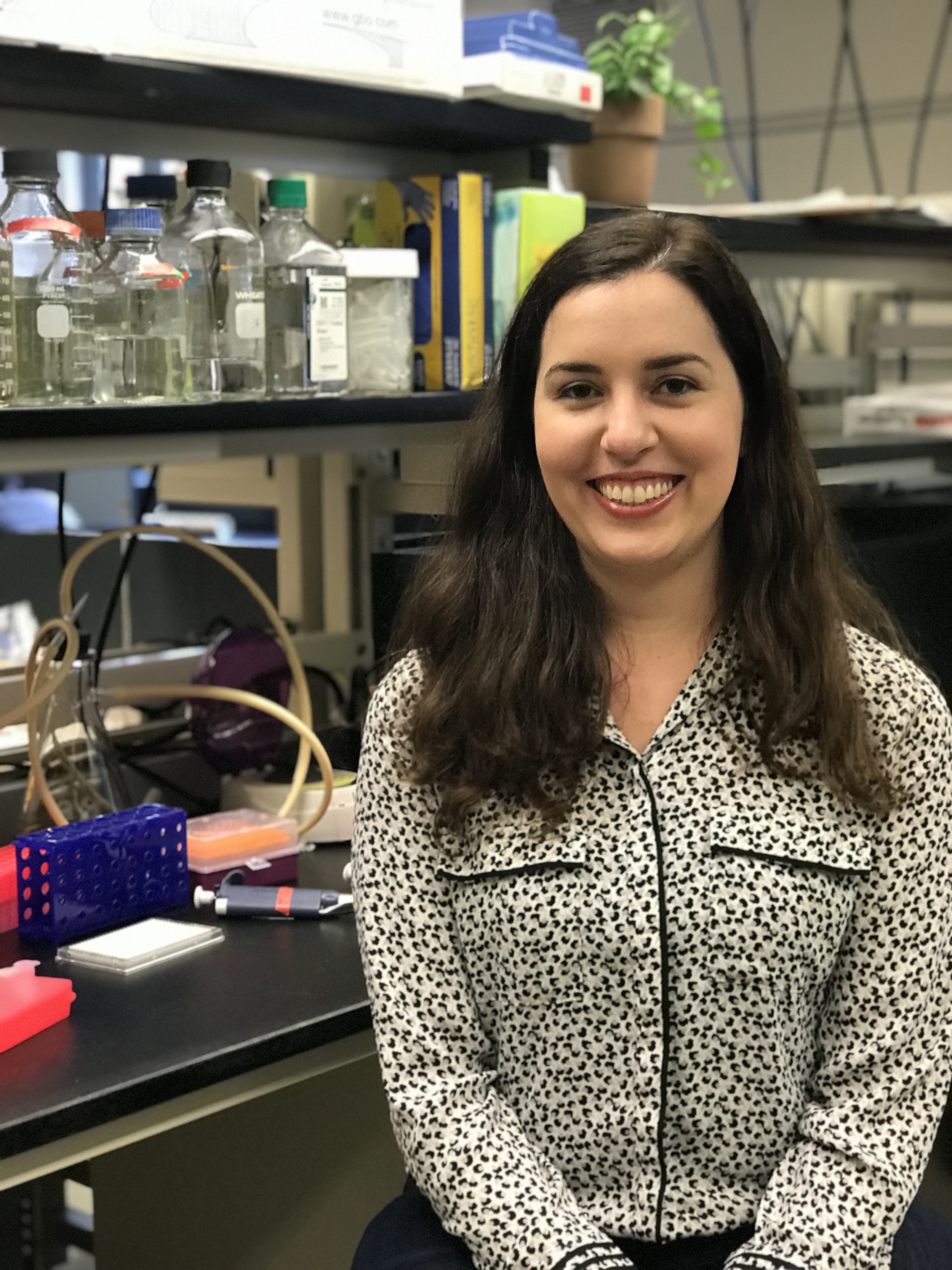 Julia Rogers A person smiling in a laboratory with various scientific equipment and supplies in the background.
