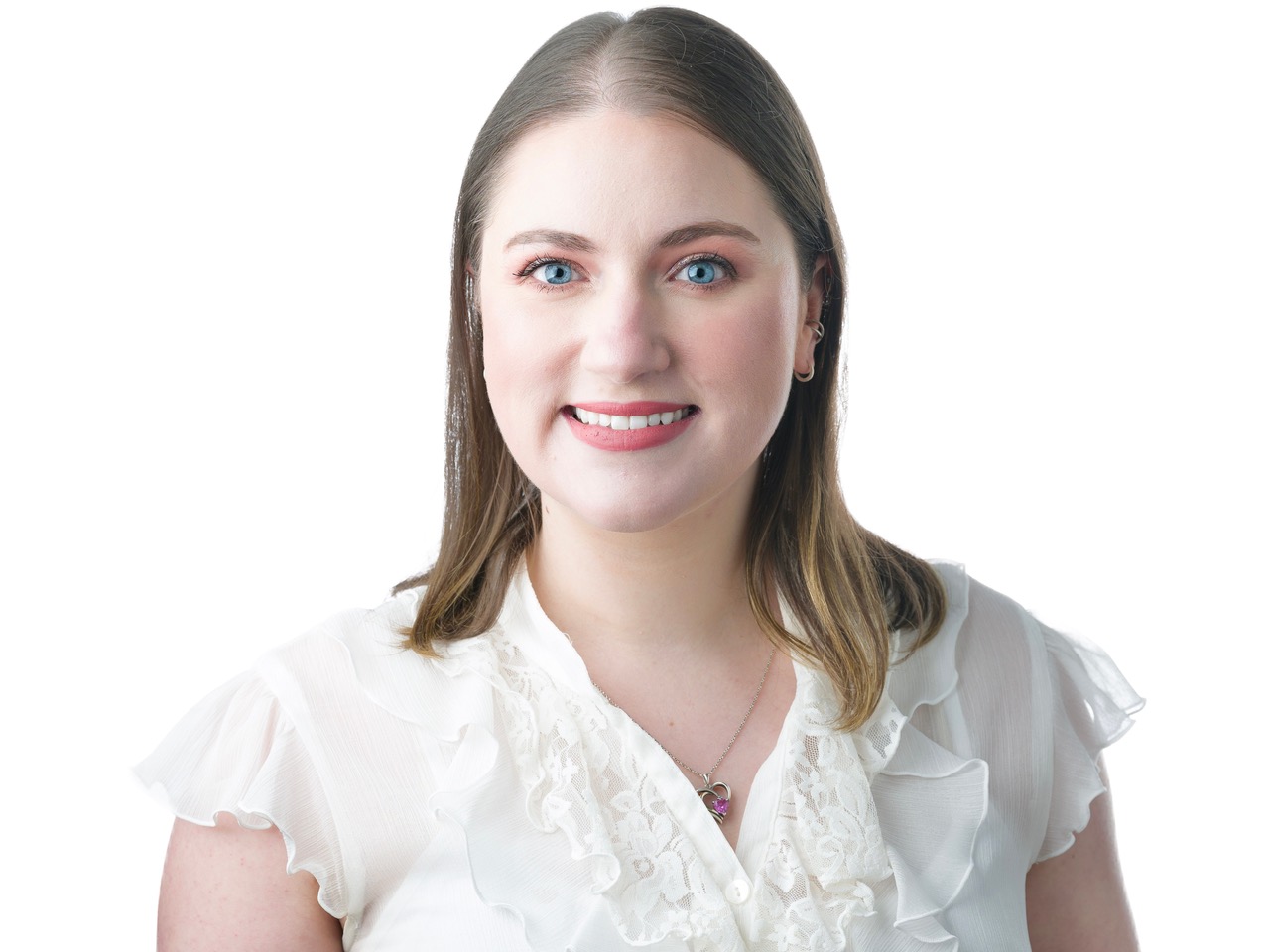 Katie Tetzloff Portrait of a smiling person with light brown hair wearing a white ruffled blouse and a heart-shaped pendant necklace.