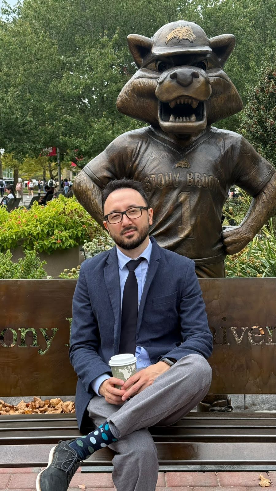 Nurlan Kabdylkhak Person sitting in front of the Stony Brook Seawolf Statue, holding a coffee cup.