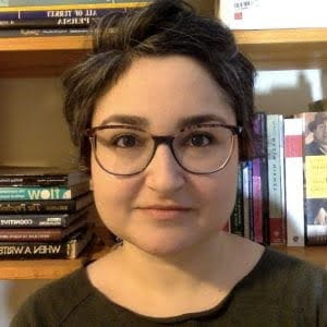 Sarah Hakimzadeh Person with short hair and glasses, standing in front of a bookshelf filled with books.