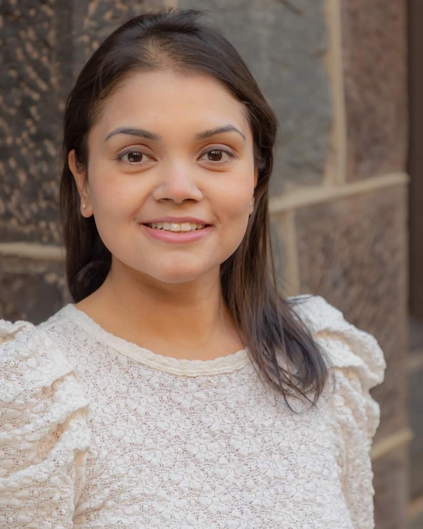 Sreeparnal Sarka A person smiling at the camera, wearing a lace top, with a textured stone wall in the background.
