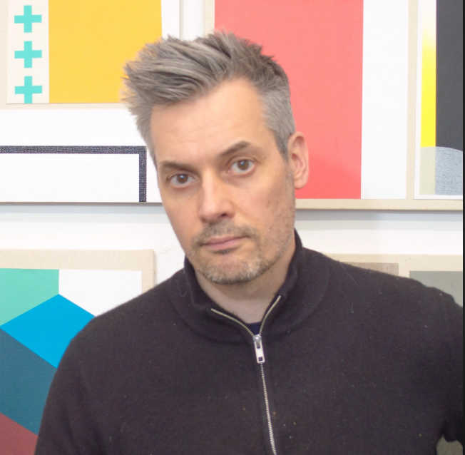 Andrew Falkowski Person with gray hair and a black zip-up sweater standing in front of colorful abstract art.