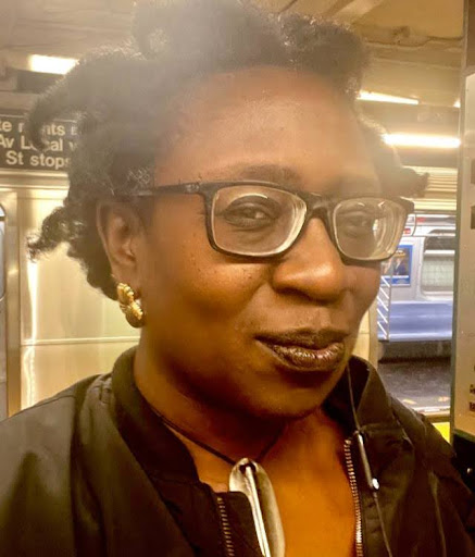 Darla Migan Person with glasses smiling inside a subway station.