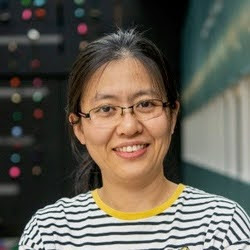 Han Ma  A portrait of an individual wearing glasses and a striped shirt, smiling in front of a blurred background with colorful lights.