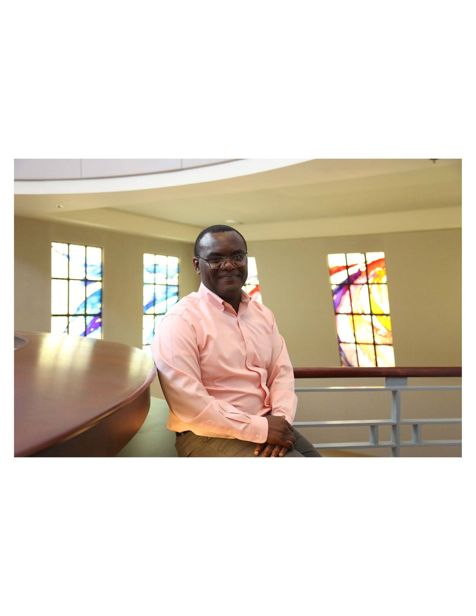 Jacques Keubeung Person sitting on a bench inside a building with large colorful stained glass windows in the background.