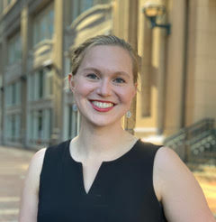 Jill Alty Smiling person in a black dress standing in front of a historical building.