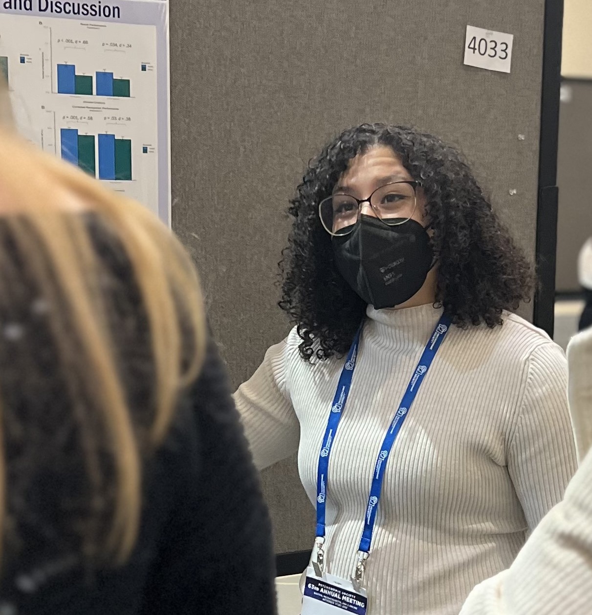 Person presenting a poster with graphs and data at a conference, wearing a mask and a lanyard, standing by poster number 4033.