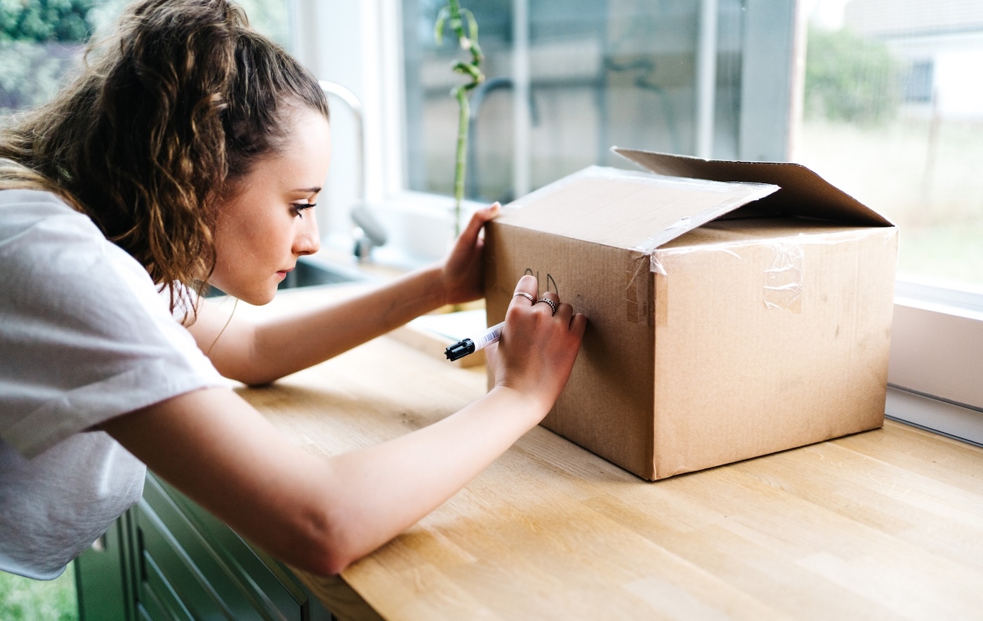 A high schooler writes on a shipping box with a Sharpie marker